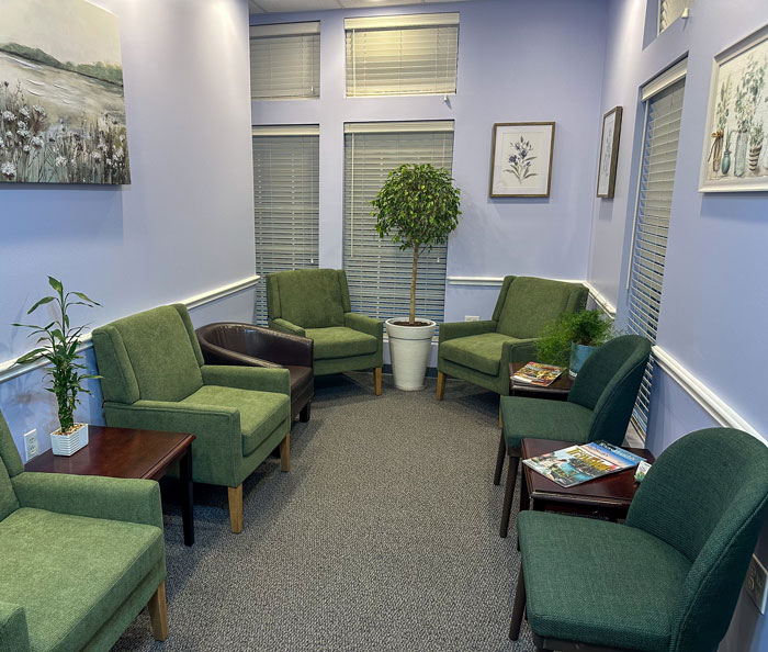 Klavy Usheva, DMD | Dental office waiting room with green chairs, soft blue walls, and framed artwork.