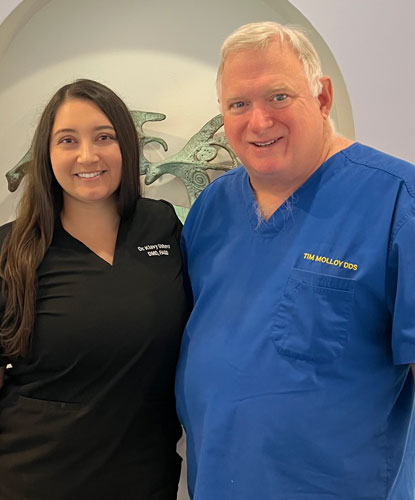 Klavy Usheva, DMD | Dr. Klavy Usheva standing beside a male dentist in blue scrubs inside a dental office.â