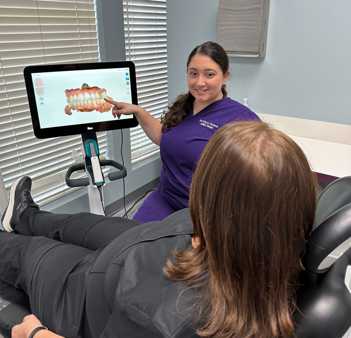 Klavy Usheva, DMD | Dr. Klavy Usheva in purple scrubs showing a patient a digital 3D model of teeth on a screen.