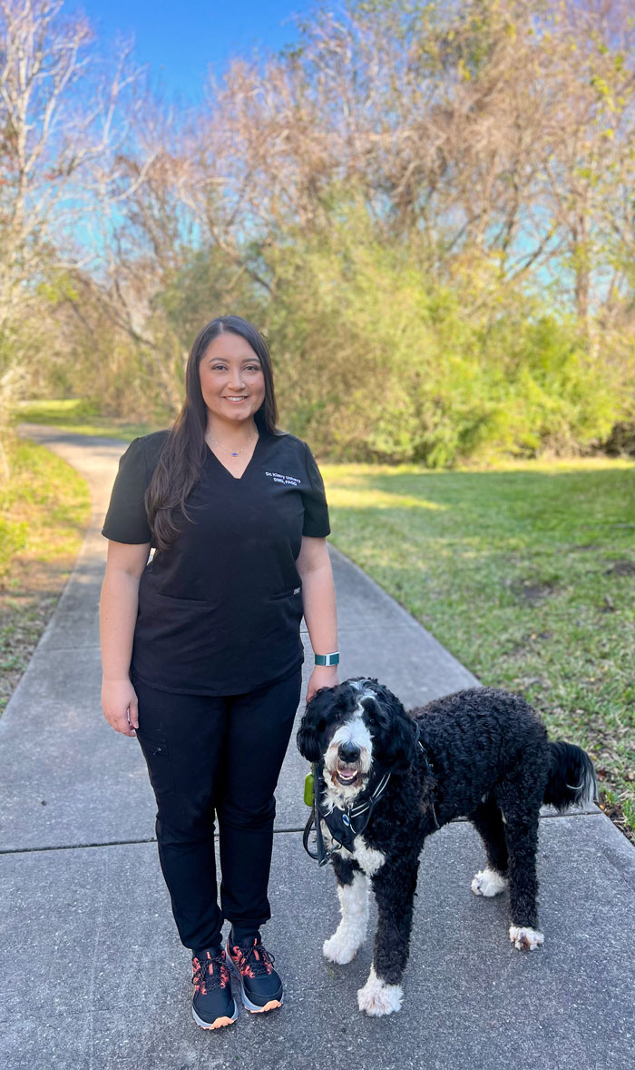 Klavy Usheva, DMD | Dr. Klavy Usheva standing on a park path with her large black-and-white dog.
