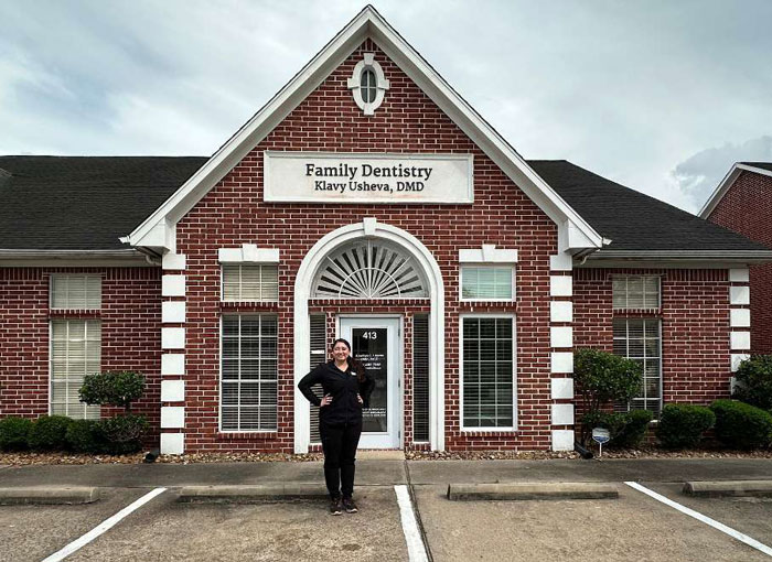 Klavy Usheva, DMD | Exterior of a red brick dental office building labeled âFamily Dentistry Klavy Usheva, DMD,â with Dr. Usheva standing in front.